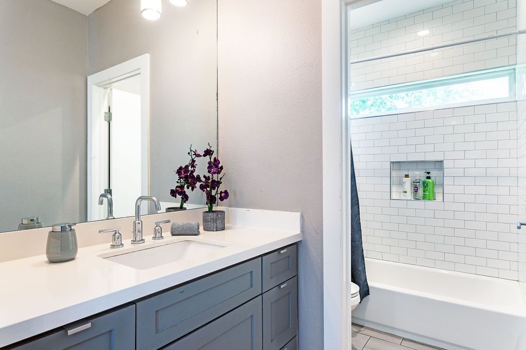 Une salle de bain moderne avec un lavabo blanc, des meubles gris, un grand miroir et une douche dotée d’une paroi en verre.