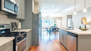 A modern kitchen with stainless steel appliances, a dining area with a table and chairs, and a view to the outside. - 3BR Comfy Bungalow 1747! Medical Center, Stadiums! ⭐️⭐️⭐️⭐️⭐️ (Houston)