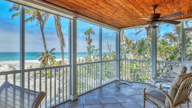 Un balcon abrité avec vue sur la plage, un ventilateur de plafond et des chaises en osier.