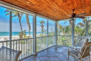 Un balcon abrité avec vue sur la plage, un ventilateur de plafond et des chaises en osier.