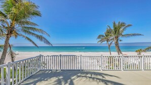 Une vue sur la plage, avec une clôture blanche, des palmiers et un ciel bleu dégagé.