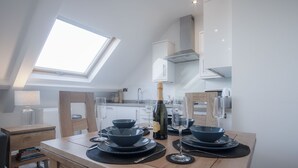 Een moderne keuken met dakraam, een houten eettafel gedekt met servies, en een fles wijn.