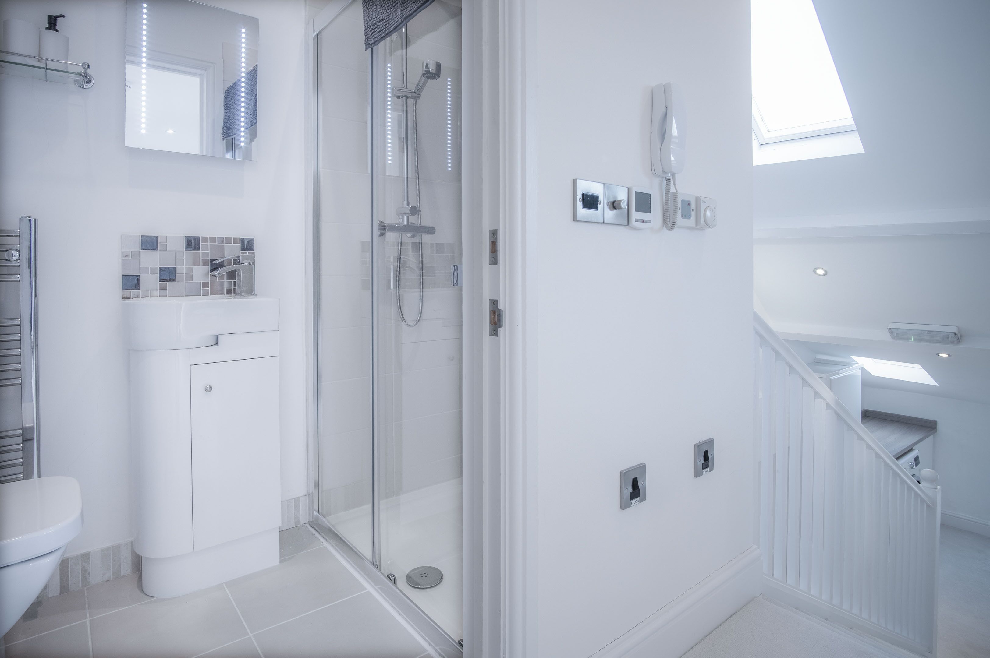 A modern bathroom with a glass-enclosed shower, a white sink, and a mirror with lights.