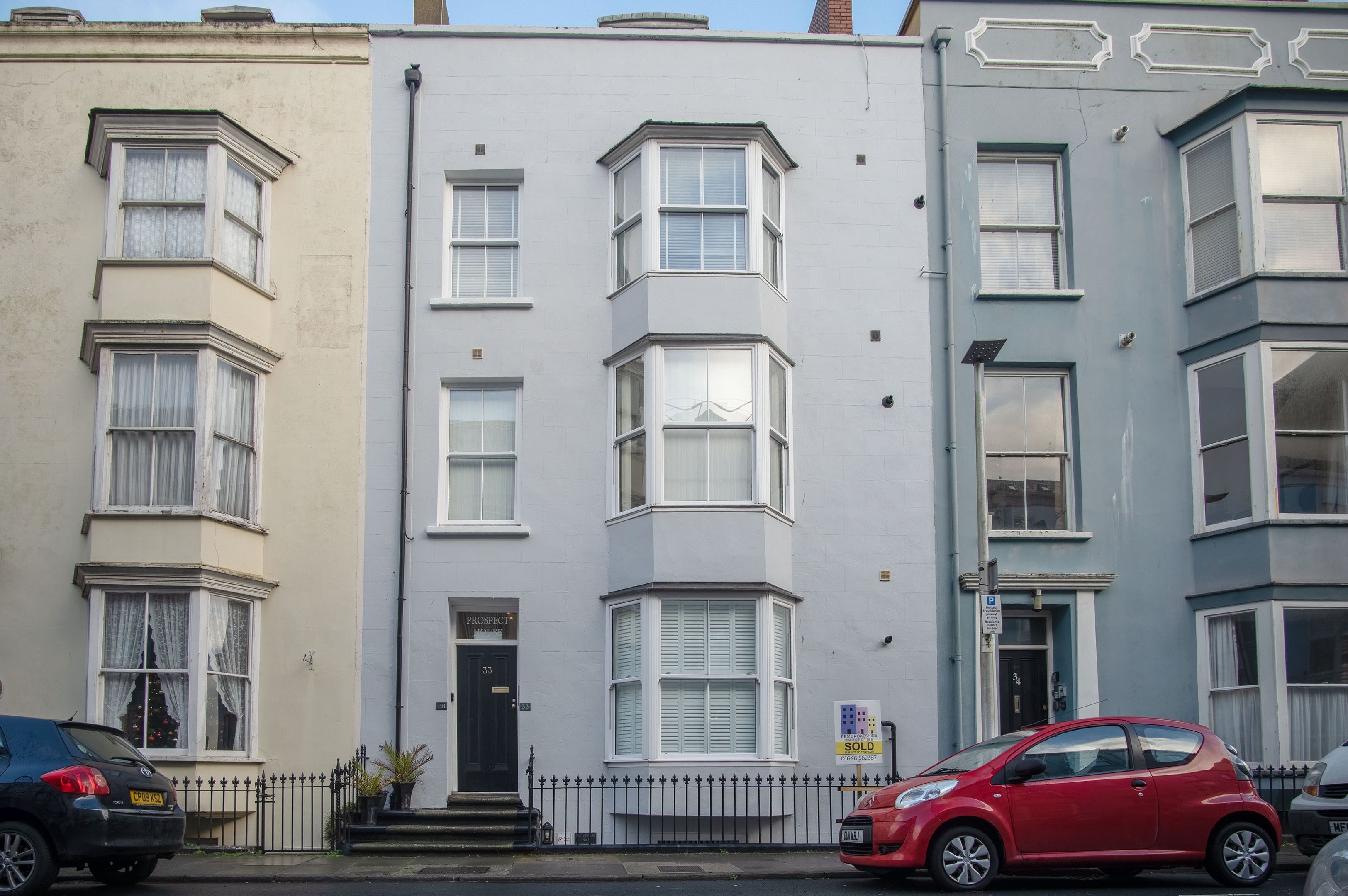 A row of three-story townhouses with bay windows, a black front door, and a 'SOLD' sign.