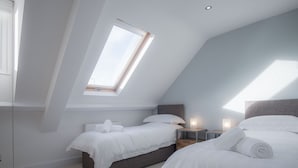 Een moderne slaapkamer met twee bedden, een dakraam en een nachtkastje met een lamp.