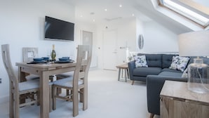 Een moderne woonkamer met een eethoek, een grijze bank en een aan de muur bevestigde televisie.