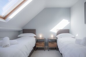 Ein modernes Schlafzimmer mit zwei Betten, einem Oberlicht, Nachttischen mit Lampen und Blick auf den Himmel.