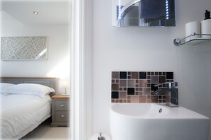 Ein modernes Schlafzimmer mit Bett, Nachttisch und einem Badezimmer mit Waschbecken und Spiegel.