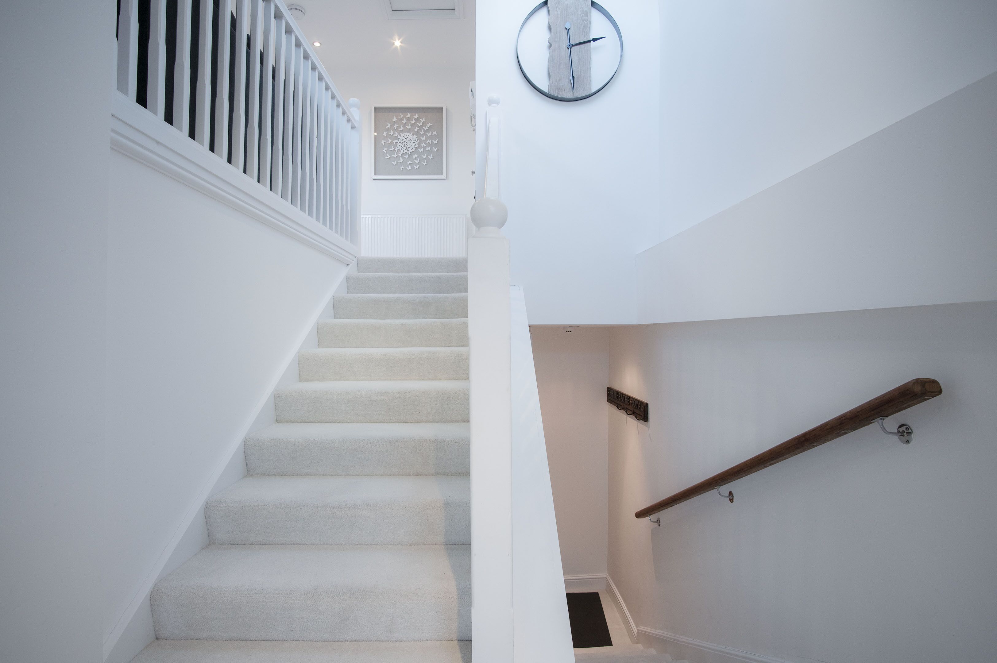 Eine Treppe mit weißen Wänden, einer Uhr und einem hölzernen Geländer.