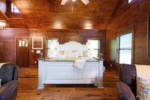 Une chambre avec un grand lit, des murs en bois, une porte et une fenêtre avec des stores.