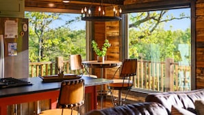 A cozy cabin interior with a wooden dining area, a sofa, and a large window offering a view of trees. - Fireplaces, hot tub, romantic cabin perfect for a honeymoon or a getaway for two (Ringold)