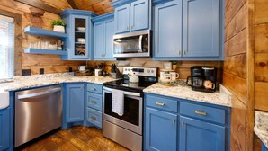 A kitchen with blue cabinets, stainless steel appliances, and a wooden ceiling. - Hot tub, fireplaces, perfect for romantic honeymoons and anniversaries, private  (Ringold)