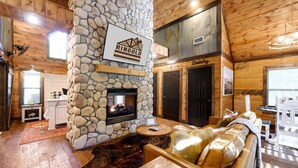 A log cabin interior with a stone fireplace, a stone wall, a wooden ceiling, and a cozy seating area. - Hot tub, fireplaces, perfect for romantic honeymoons and anniversaries, private  (Ringold)