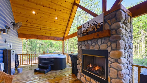 A covered outdoor deck with a stone fireplace, a hot tub, and a wooden ceiling. - Hot tub, fireplaces, perfect for romantic honeymoons and anniversaries, private  (Ringold)