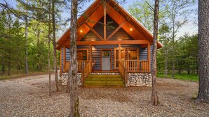 A log cabin with a stone foundation, wooden deck, and a porch with railings. - Hot tub, fireplaces, perfect for romantic honeymoons and anniversaries, private  (Ringold)