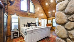 A bedroom with a white bed, a stone wall, and a wooden ceiling. - Hot tub, fireplaces, perfect for romantic honeymoons and anniversaries, private  (Ringold)