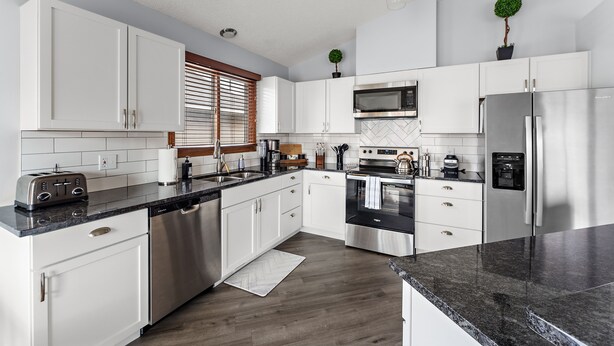 Una cocina moderna con armarios blancos, electrodomésticos de acero inoxidable y encimera de granito.