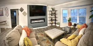 A living room with a fireplace, a television, and a seating area with cushions.
