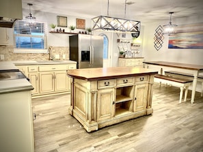 A kitchen with a central island, wooden cabinets, a refrigerator, and a dining area with a bench.