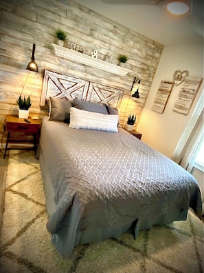 A bedroom with a bed, nightstands, a wall-mounted shelf, and a decorative headboard.