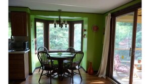 Uma área de refeições com mesa e cadeiras, um lustre e vista para um deck externo através de uma porta de vidro deslizante.