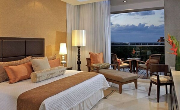 Relax in a spacious room with a large bed, wooden nightstand, and a seating area offering a view of the surrounding landscape.