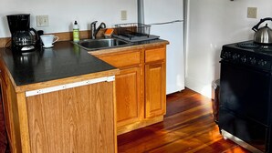 Een keuken met houten kastjes, een zwart aanrecht, een roestvrijstalen spoelbak, een magnetron, een koelkast, een fornuis en een klok aan de muur.