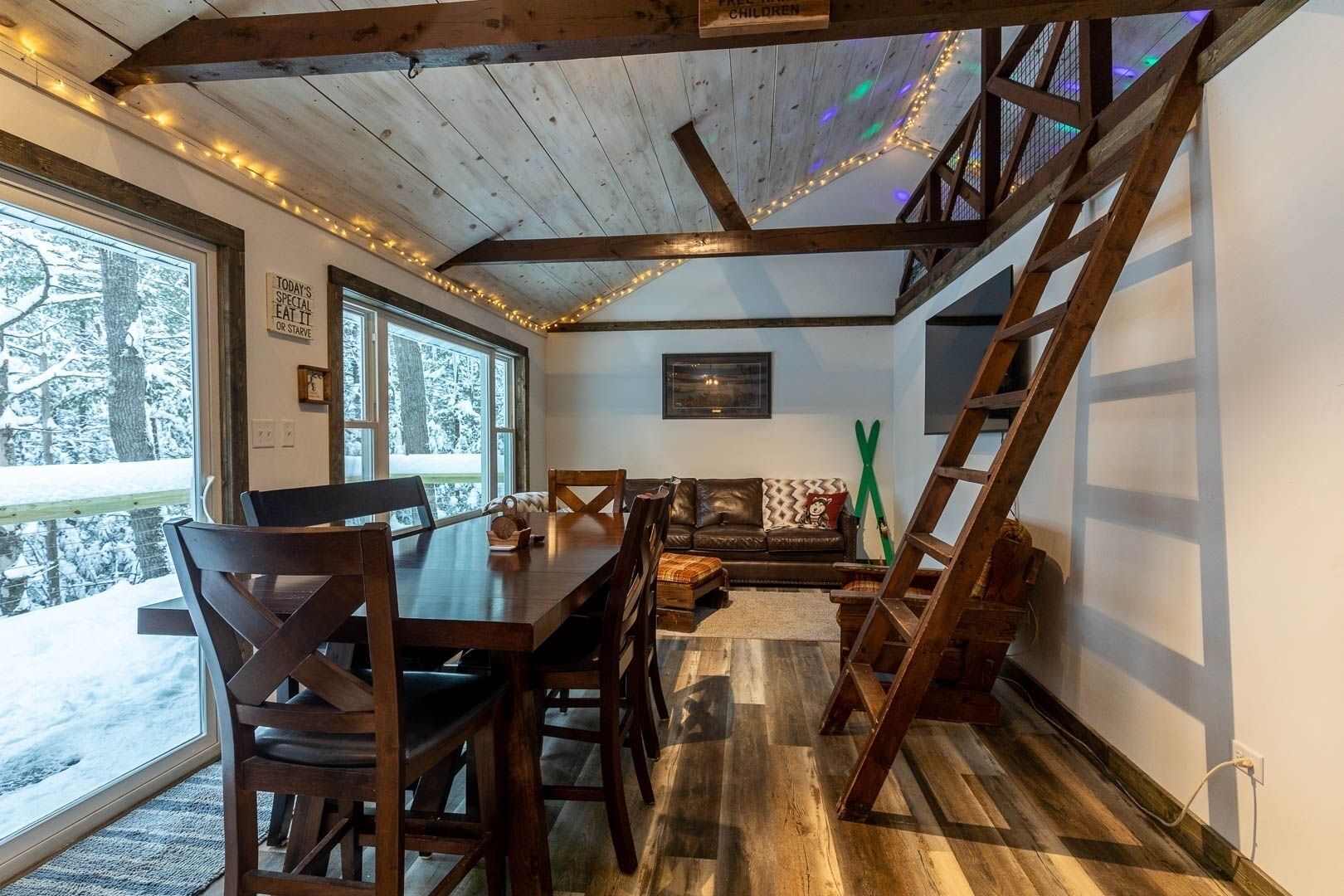 Een gezellig chaletinterieur met een eettafel, stoelen, een bank en een trap.