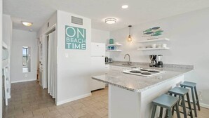 Una cocina moderna con una isla central, horno empotrado y un lavabo. En la pared hay un cartel que dice "ON BEACH TIME".