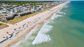 Vista aérea de una playa con una hilera de edificios, incluyendo Ocean Grill & Tiki Bar, a lo largo de la costa.