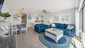 Una sala de estar moderna con un sofá azul, una mesa de centro blanca y un comedor con una mesa y sillas blancas.