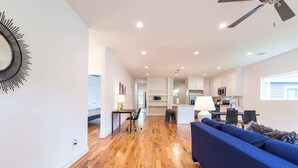 A modern living room with a blue sofa, wooden flooring, and a ceiling fan. - 3BR Cozy Bungalow 1749! Medical Center, Stadiums! (Houston)