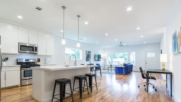 A modern kitchen with white cabinets, stainless steel appliances, and a central island with bar stools. - 3BR Cozy Bungalow 1749! Medical Center, Stadiums! (Houston)