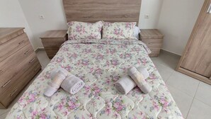 Ein Schlafzimmer mit einem Bett, einer Holzkommode, Nachttischen und einem Kleiderschrank.
