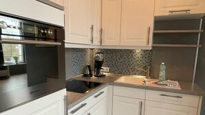 Eine moderne Küche mit weißen Schränken, einem eingebauten Backofen, einer Kaffeemaschine und einem Edelstahlkühlschrank.