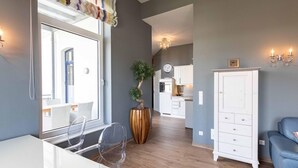 Ein modernes Wohnzimmer mit großem Fenster, einer Topfpflanze, einem weißen Schrank und einem blauen Sofa.