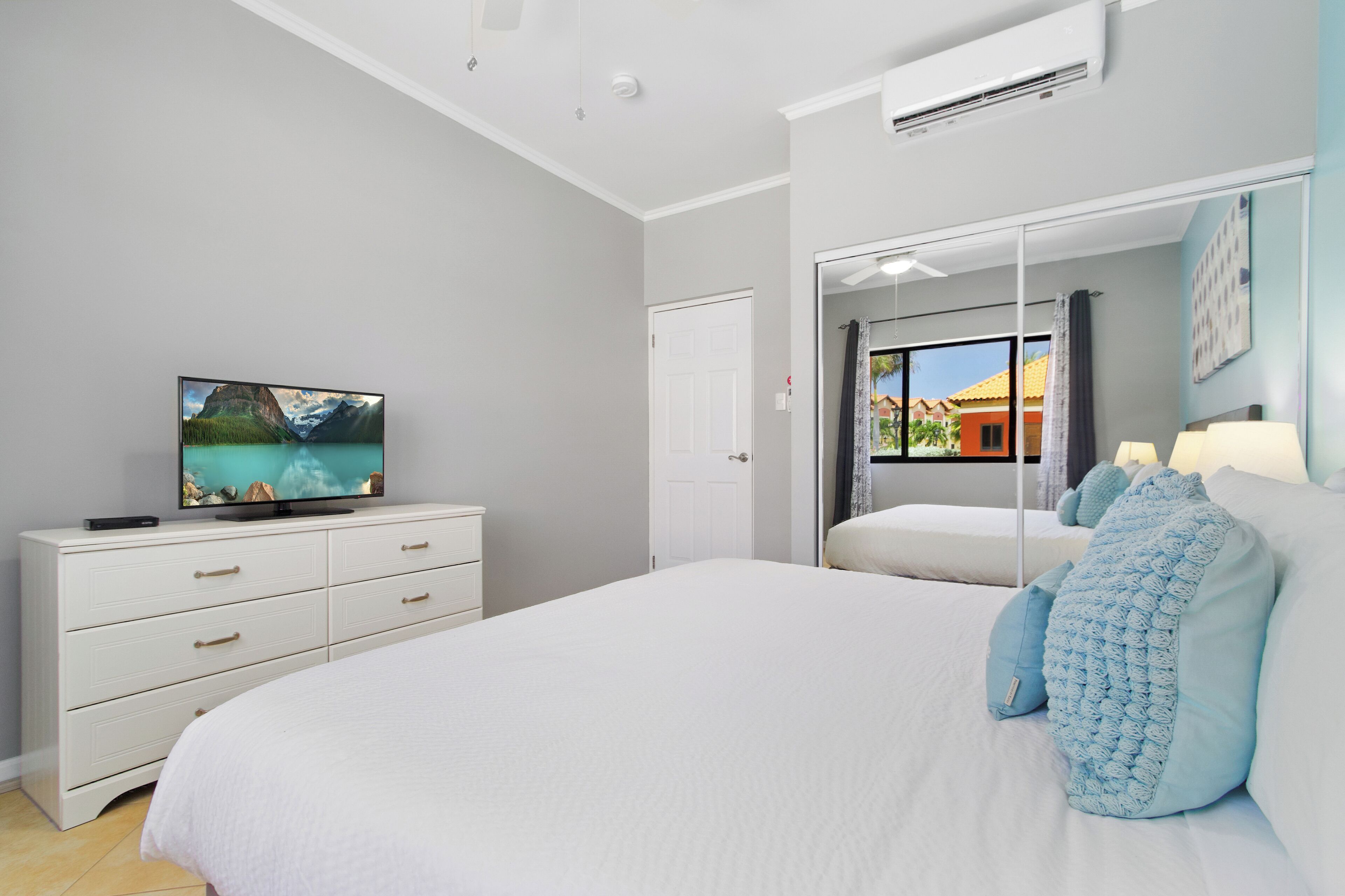 Une chambre à coucher avec un grand lit, une commode, une télévision et un miroir.