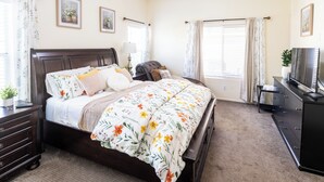 Een slaapkamer met een bed, nachtkastjes, een dressoir, een televisie en een raam met gordijnen.