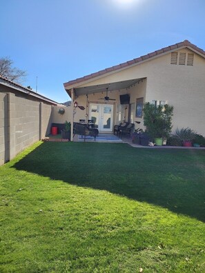 A house with a covered patio, a lawn, and a door leading to a garage.