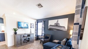 Een woonkamer met een grijze kast, een televisie, een bank en een schilderij van de Eiffeltoren.