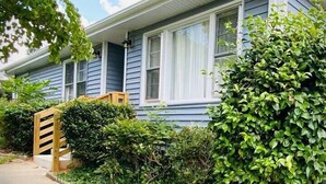 Een tweelaags huis met een veranda, een houten bank en een verzorgde tuin.