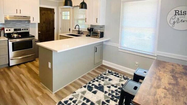 Een moderne keuken met witte kasten, een centraal eiland, roestvrijstalen apparatuur, hanglampen en een gekleurd vloerkleed.