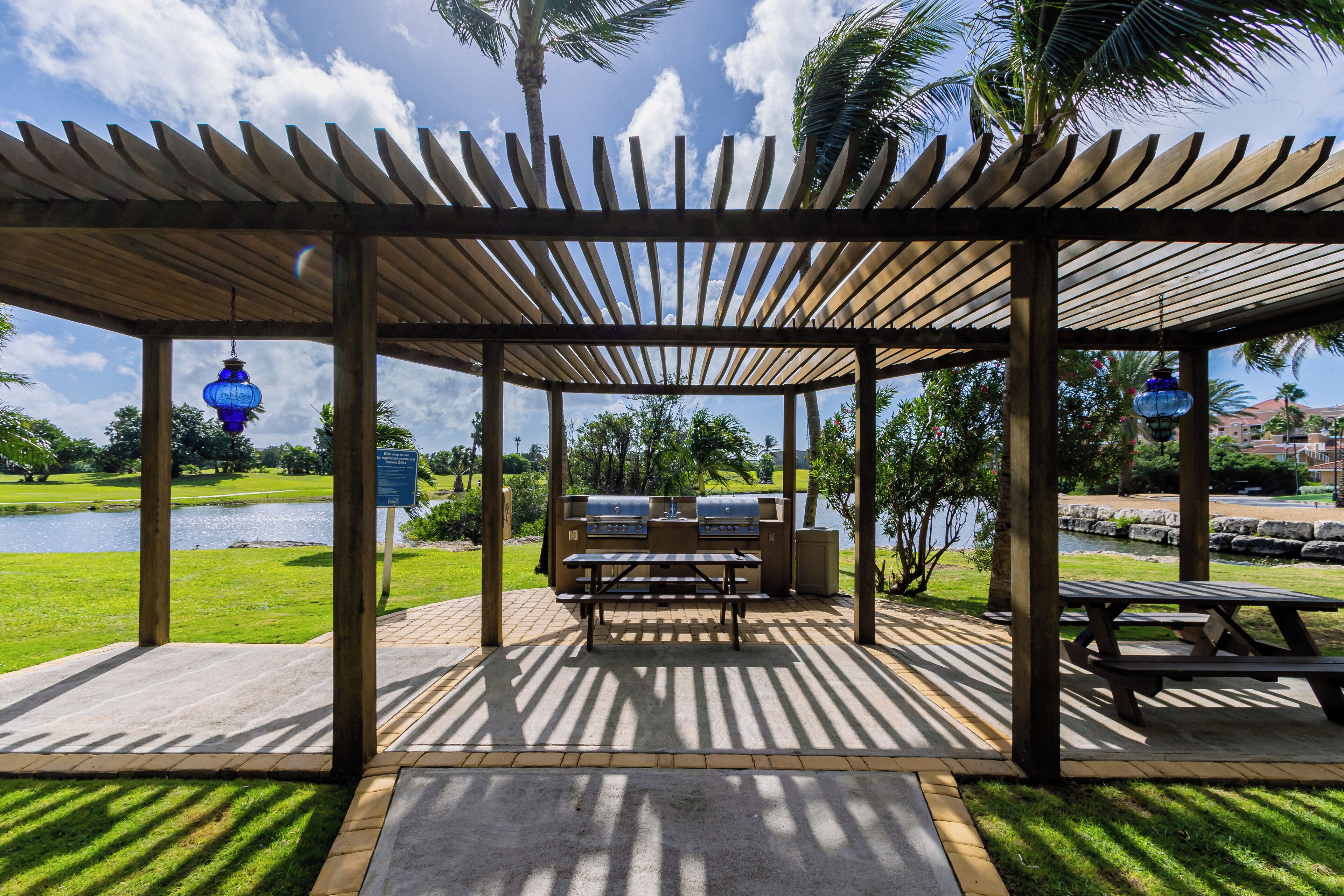 A covered picnic area with tables and grills, overlooking a body of water and greenery.