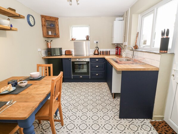 A compact kitchen with a wooden dining table, a built-in oven, and a sink. - Llety Bach (Caernarfon)