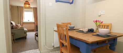 A dining area with a wooden table and chairs, a blue wall-mounted rack with baskets, and a window with curtains.