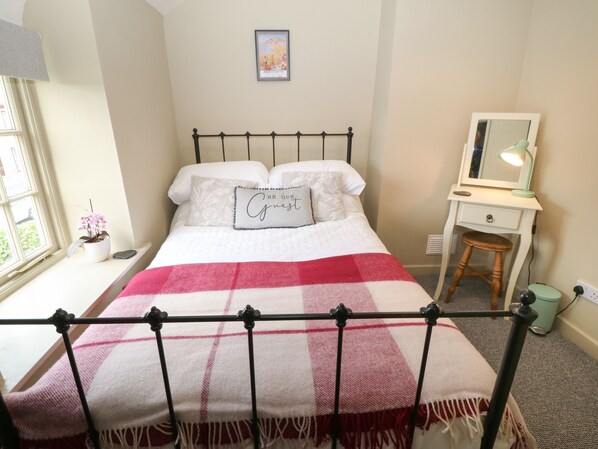 Un dormitorio ordenado con cama, mesita de noche con lámpara, cómoda y ventana con vistas.