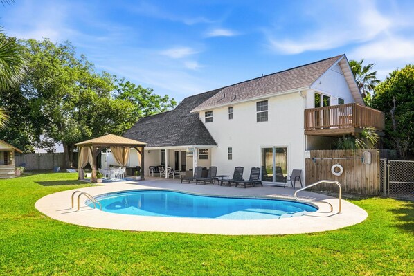 Una casa de dos pisos con piscina, un porche cubierto y una terraza de madera.
