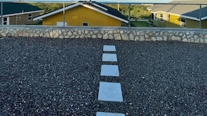 Un sendero de grava que conduce a un edificio amarillo con un muro de piedra al frente.