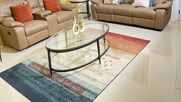 Un salón amplio con dos sofás de cuero, una mesa de centro de vidrio y una alfombra colorida.