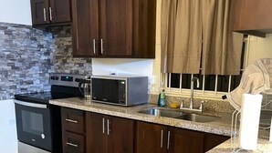 Una cocina con armarios de madera oscura, encimera de granito, microondas, estufa y una ventana con cortinas.